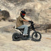 Helmeted rider positioned on Freego X0 mini e-bike, resting on sunlit rocky terrain.