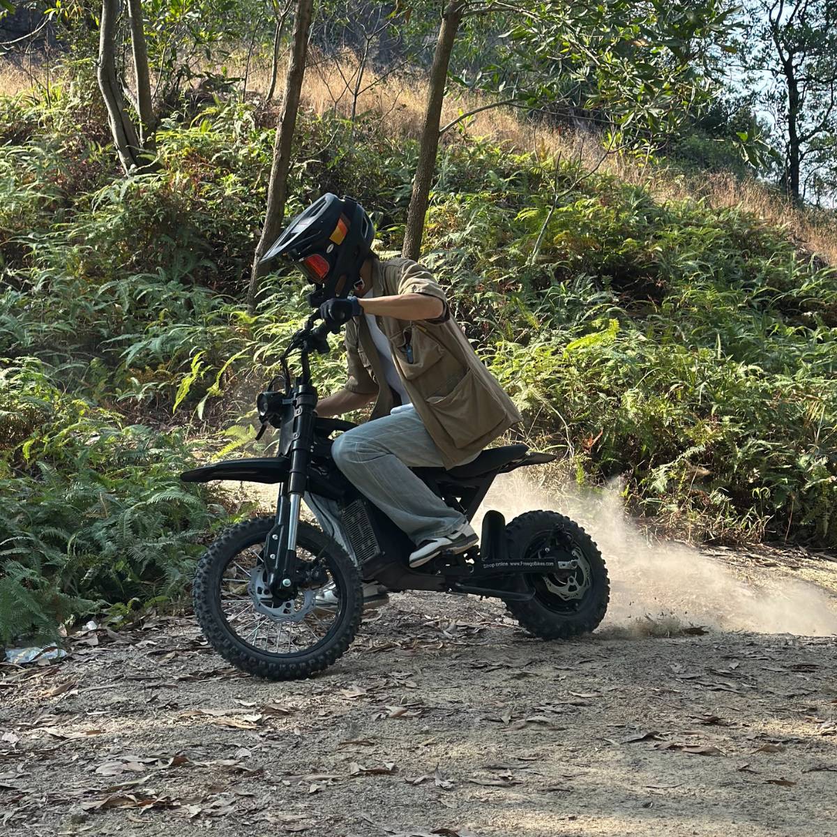 Helmeted rider on Freego X0 mini e-bike, kicking up dust on a wooded dirt trail.
