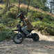 Helmeted rider on Freego X0 mini e-bike, kicking up dust on a wooded dirt trail.
