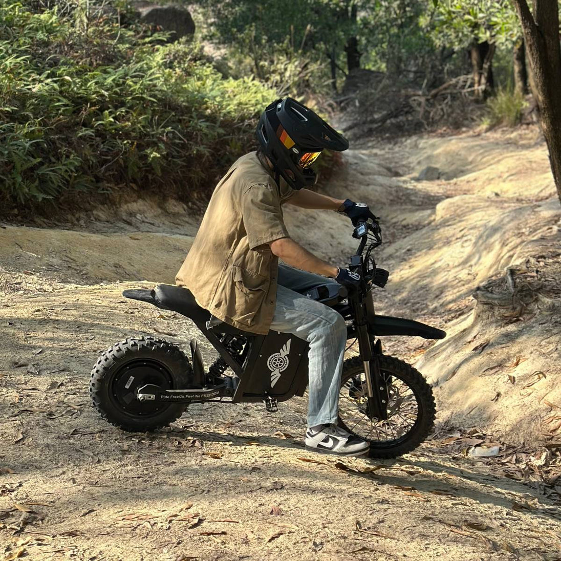 Rider on Freego X0 electric mini dirt bike navigating a wooded dirt trail.