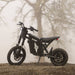 A Freego X0 electric dirt bike parked on a gravel path during a foggy morning, showcasing its rugged frame.