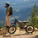 Person with a backpack standing next to a Freego X2 Pro dirt ebike on a mountainous landscape