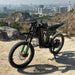 Freego X3 electric dirt bike is parked on a rocky hill at the city’s edge; its rugged tires and brand logo stand out, with urban buildings and quarried terrain in the backdrop.