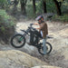 Freego X3 electric dirt bike navigates a rocky gully in a forested area; helmeted rider balances the bike, with ferns and trees lining the uneven trail.