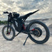 Freego X3 electric dirt bike (with pedals) parked on rocky terrain, dramatic sky backdrop; brand logos and rugged tires visible.